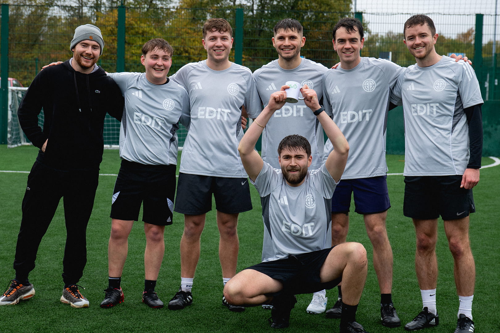 Photograph from Cup North 25. Winners, EDIT Studio hold their trophy (a small mug) above their head.